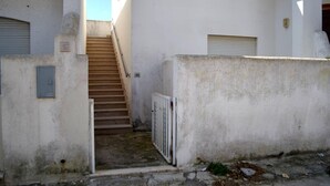 Una estrecha escalera conduce a una entrada protegida por un portón metálico y un pequeño cuadro eléctrico en la pared.
