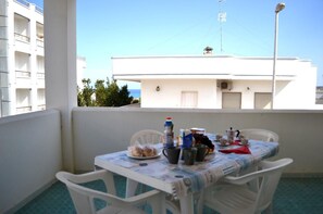 A balcony with a table set for breakfast, white chairs, and a view of a building with balconies and a clear sky.