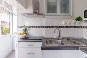 Uma cozinha moderna com armários brancos, uma pia de aço inoxidável, fogão embutido e uma janela com vista.