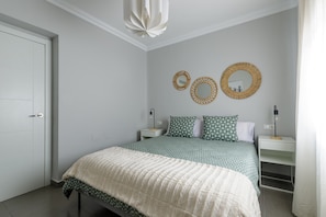 Une chambre à coucher comprenant un lit, deux tables de chevet, une commode, un miroir fixé au mur et une porte.