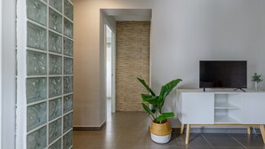 Una sala de estar moderna con un muro de bloques de vidrio, un mueble blanco con un televisor, una planta grande y suelo de madera.