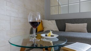 Una mesa de vidrio con una copa de vino y un plato de comida, un sofá con cojines, y un libro sobre la mesa.