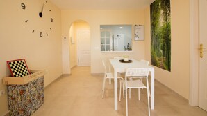 Una habitación de hotel con zona de comedor, un reloj de pared, un tablero de ajedrez y un cuadro.