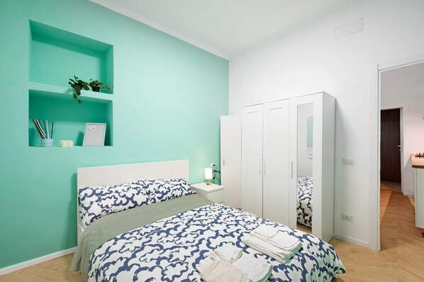 A bedroom with a bed, a nightstand, a wardrobe, and a shelf with plants.