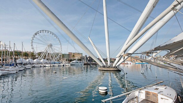 Un puerto deportivo con barcos amarrados, una noria al fondo y un velero grande con varios palos.
