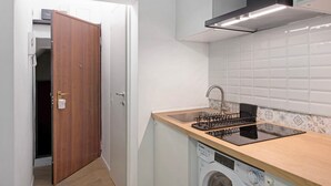Una cocina compacta con lavadora incorporada, una puerta de madera y salpicadero de azulejos.