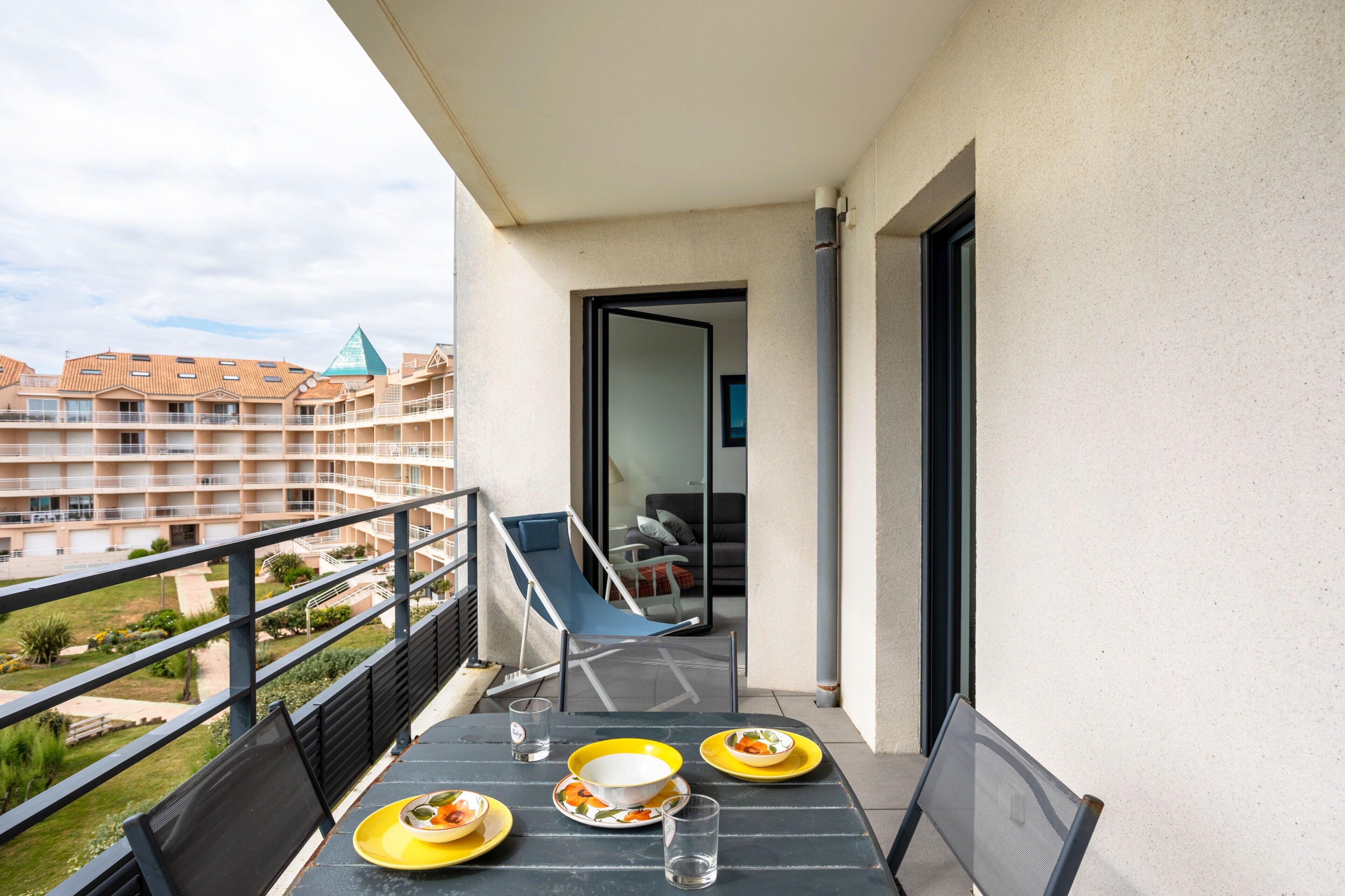 A balcony with a table set for two, a chair, and a view of a building with a pyramid-shaped roof.