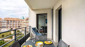 A balcony with a table set for two, a chair, and a view of a building with a pyramid-shaped roof.