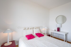 A neatly arranged bedroom with a bed, two bedside tables, a nightstand, a white console table, and a round mirror.