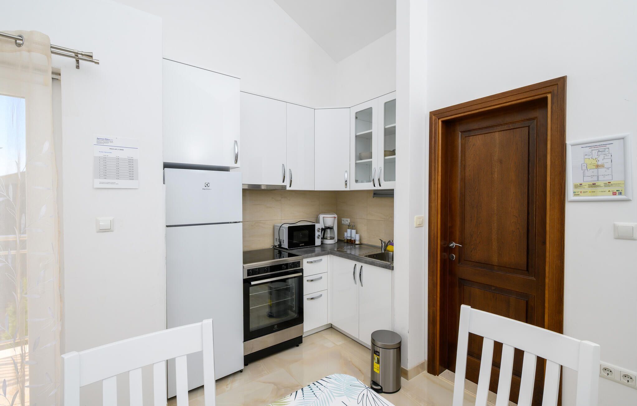 A compact kitchen with white cabinets, a microwave, a coffee maker, and a trash bin.