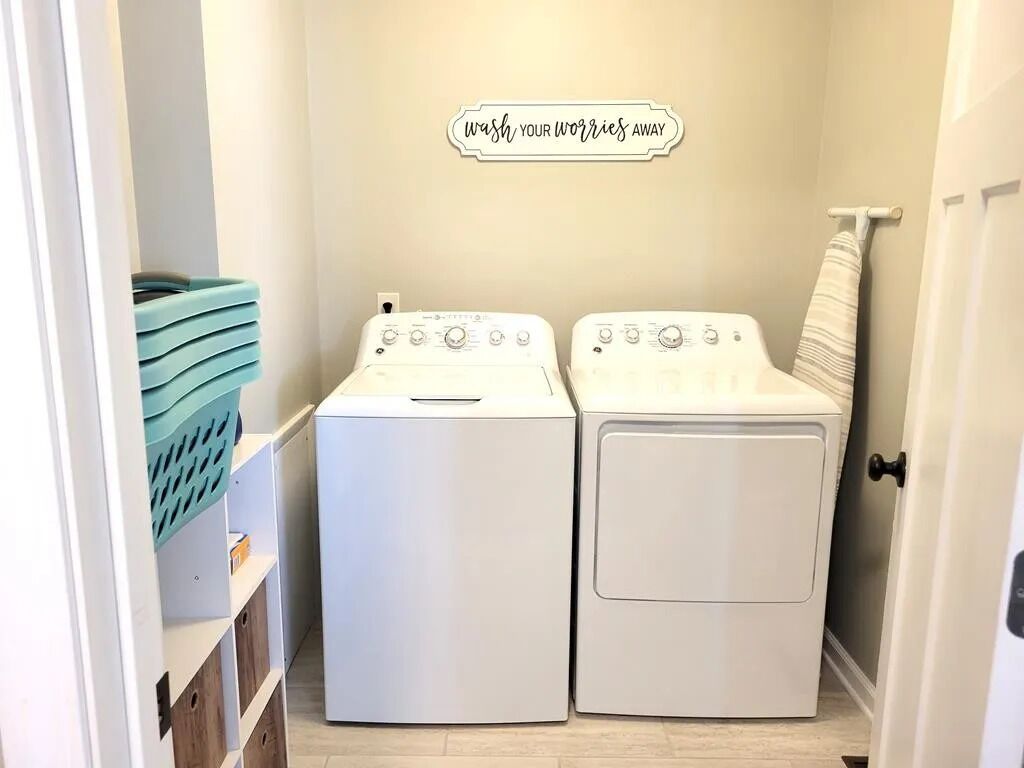 A laundry room with two white front-loading washing machines, a wall-mounted towel rack, and a sign that reads "wash your worries away."