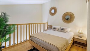 Ein Schlafzimmer mit einem hölzernen Bett, einem Nachttisch mit Lampe, zwei Wandspiegeln und einer Topfpflanze.