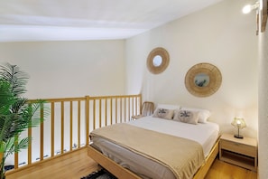 A bedroom with a wooden bed, a nightstand with a lamp, two wall mirrors, and a potted plant.