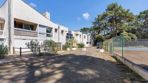Ein Wohngebäude mit Kiesweg, Tennisplatz und umliegenden Bäumen.