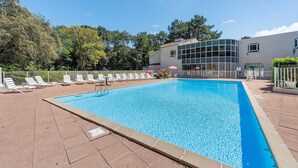 Ein rechteckiger Swimmingpool mit Fliesen umgeben, mit weißen Liegestühlen und Sonnenschirmen.