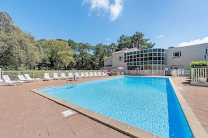 A rectangular swimming pool with a tiled deck, surrounded by white lounge chairs and umbrellas.