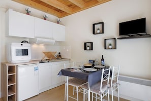 Une cuisine compacte avec des meubles blancs, un four encastré, un petit réfrigérateur et un coin repas comprenant une table et des chaises.