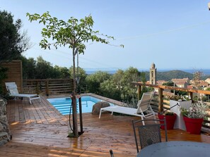 Eine Holzterrasse mit Pool, Liegestühlen und Blick auf eine Stadt und Berge.