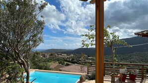 A wooden deck with a pool, overlooking a village and mountains.