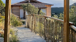 A wooden pergola leading to a house with a tiled roof, surrounded by natural landscape.