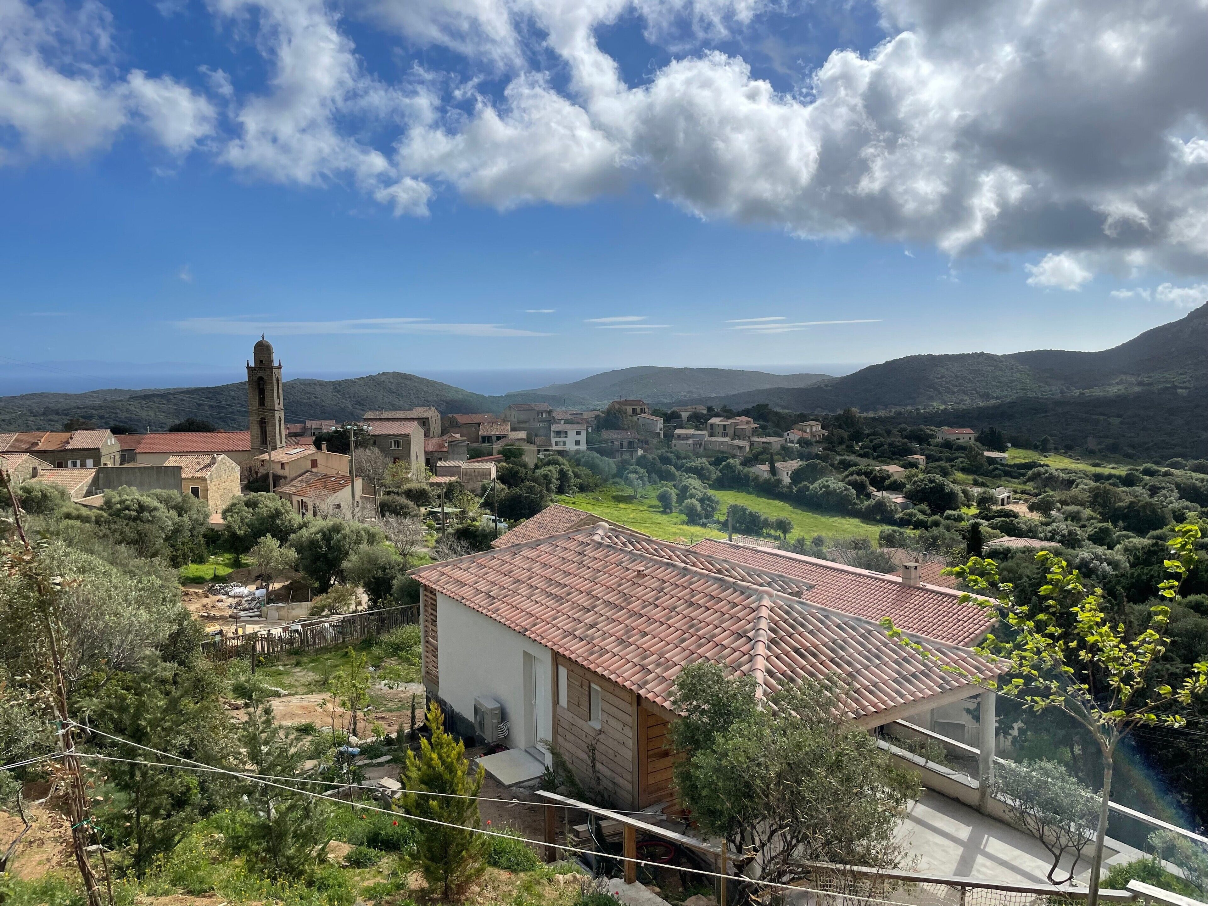 A rural village with traditional architecture, including a church with a bell tower, surrounded by greenery and hills.