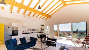 A modern interior with a wooden ceiling, a sofa, a dining table, and a view through large windows.
