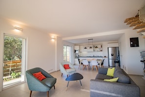 Un espacio habitable moderno con comedor, cocina y un amplio ventanal corredero a un jardín.