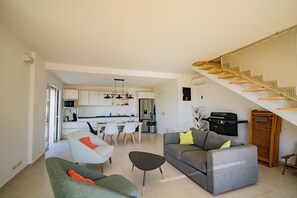 A modern living room with a grey sofa, a green armchair, and a black ottoman. There is a staircase with a wooden railing and a white wall.