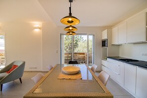 A modern kitchen with white cabinets, a black countertop, and a dining area with a woven table mat and chairs.