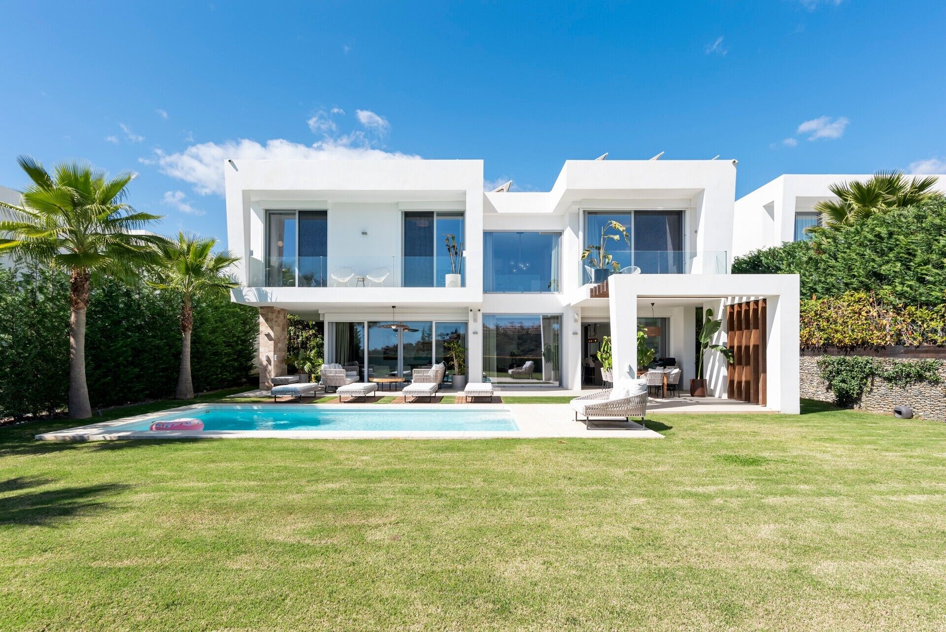 A modern two-story house with a swimming pool, outdoor seating, and lush greenery.