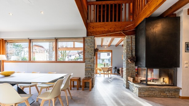 A spacious dining area with a long table and chairs, a stone fireplace, and large windows offering a view of the outside. - Chalet 'Pierre Et Bois' with Mountain View, Private Terrace and Wi-Fi (AIGUEBLANCHE)