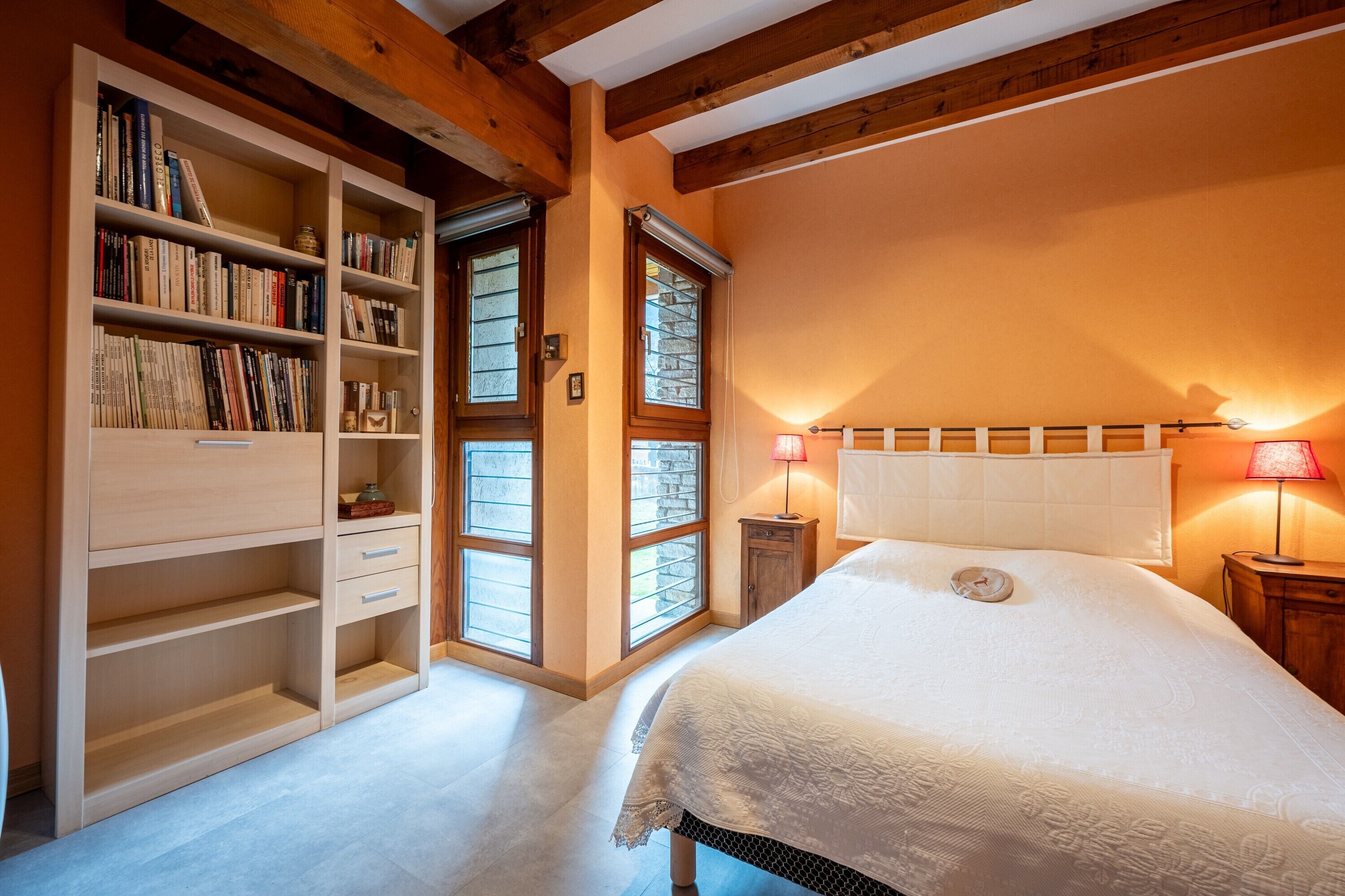 A bedroom with a large bed, a wooden bookshelf, and a window with a view.