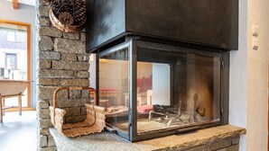 A stone fireplace with a glass enclosure, a woven basket, and a wooden chair. - Chalet 'Pierre Et Bois' with Mountain View, Private Terrace and Wi-Fi (AIGUEBLANCHE)