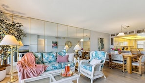 Uma sala de estar com sofá, poltronas, mesa de centro e um espaço de refeições com cadeiras e mesa.