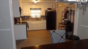 A modern kitchen with white cabinets, a black refrigerator, and a dining area with a wooden table and patterned chair. - CLOSE TO FT JACKSON, WILLIAMS-BRICE STADIUM, VA HOSP, FAMILY FRIENDLY. SLEEPS 10 (Columbia)