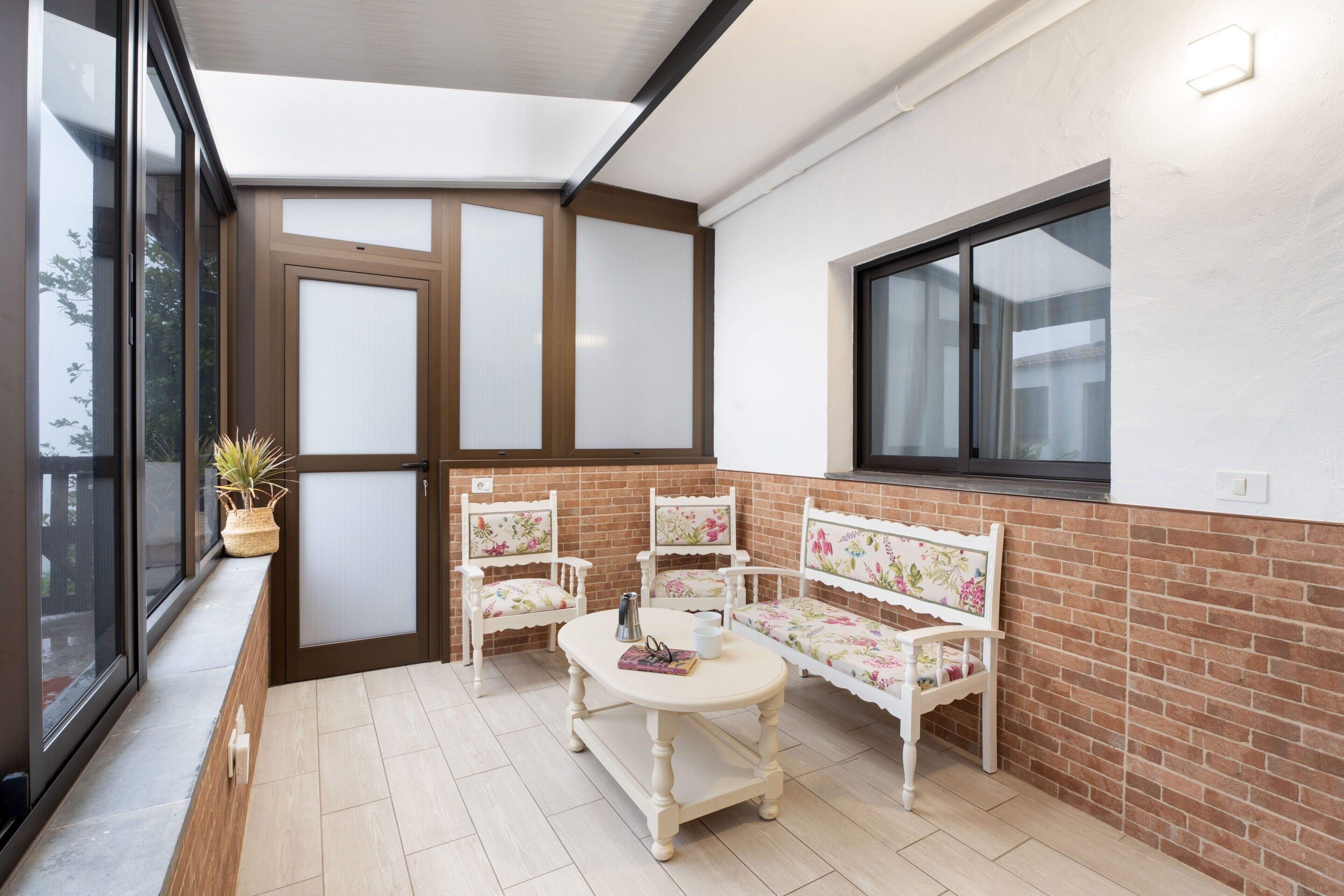 A sunlit balcony with a wooden bench, two chairs, and a small table.