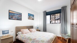 A bedroom with a bed, bedside tables, a chair, a window with curtains, and two wall-mounted paintings. - Apartment 'Casa El Isleño' with Sea View, Private Terrace and Wi-Fi (Villa de Valverde)