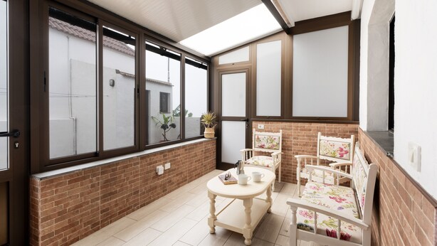 A room with a brick wall, a large window, a wooden table with chairs, and a potted plant. - Apartment 'Casa El Isleño' with Sea View, Private Terrace and Wi-Fi (Villa de Valverde)