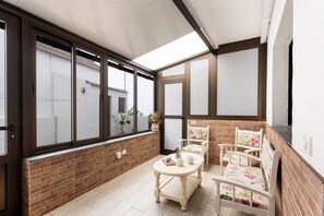 A room with a brick wall, a large window, a wooden table with chairs, and a potted plant.