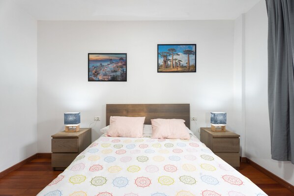 A bedroom with a bed, two bedside tables, two lamps, two pillows, and two framed pictures on the wall.