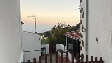 A narrow alleyway with a gated entrance, a small outdoor seating area, and a view of a distant landscape.