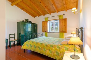 A bedroom with a bed, a nightstand, a lamp, a window with curtains, a green wardrobe, and a chair.