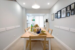 A dining area with a wooden table, chairs, a white ceiling light, and framed artwork on the wall.