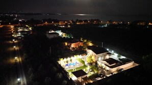 Vista nocturna d'una zona costanera amb edificis il·luminats, una piscina i una vista clara del mar.