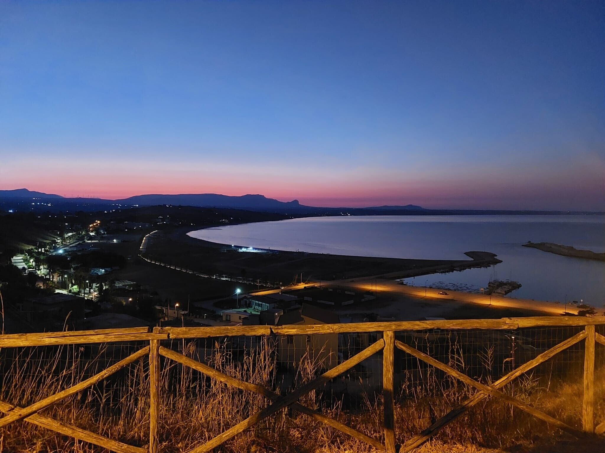 A coastal landscape at dusk with a wooden fence in the foreground.