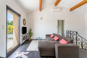 Un salon avec un canapé, un téléviseur, une plante et une vue à travers une porte vitrée.