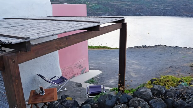 Eine Holzpergola mit Blick aufs Meer, eine rosa Wand und zwei Lounge-Sessel.
