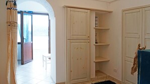 Ein Zimmer mit weiß gefliestem Boden, einer Holztür, einem weißen Schrank mit Regalen und einem blauen Vorhang.