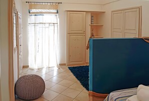 A room with a bed, a wardrobe, a small shelf, and a window with curtains.
