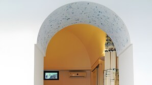 Ein rundbogiges Portal führt in einen Raum mit einem Bett, einem Sessel und einem Fernseher.
